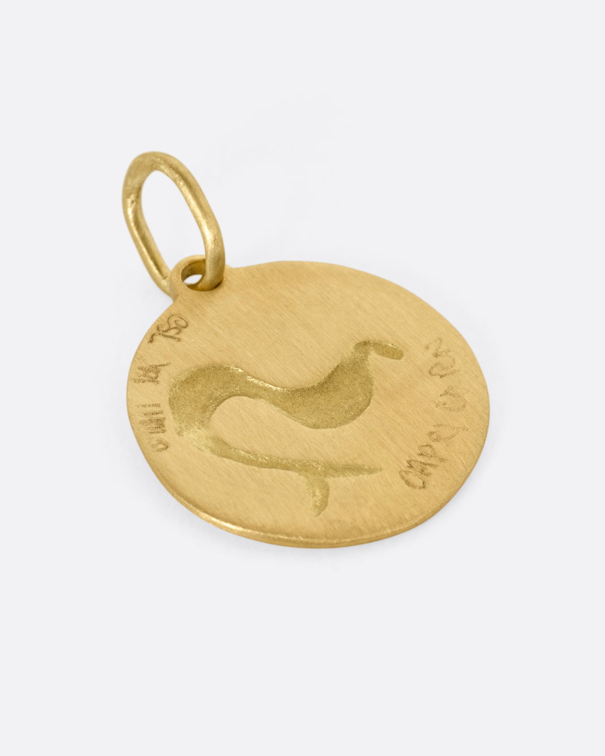 A circular yellow gold Capricorn pendant with a sea goat, shown from the back.