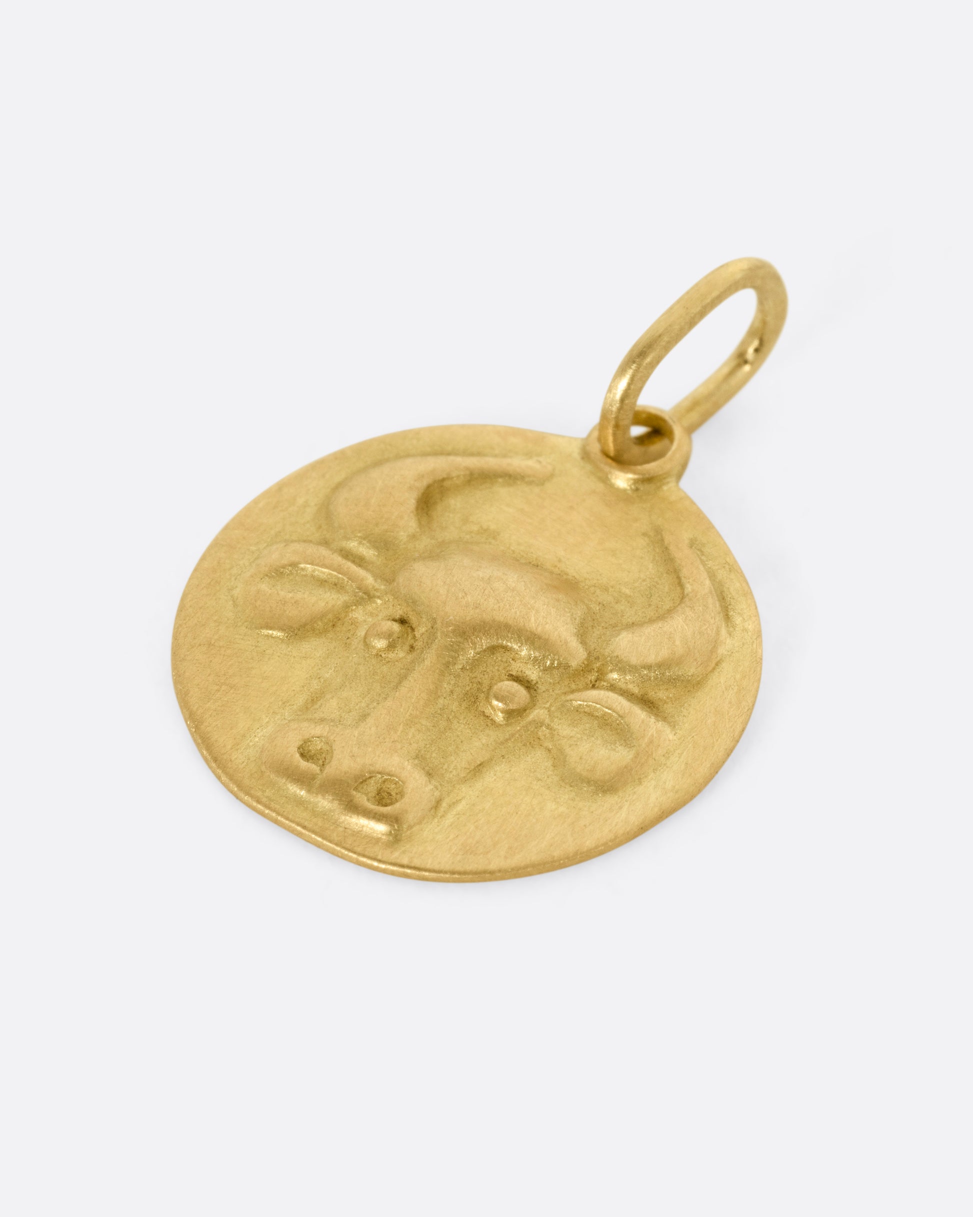 A circular yellow gold Taurus pendant with a bull head, shown from the side..