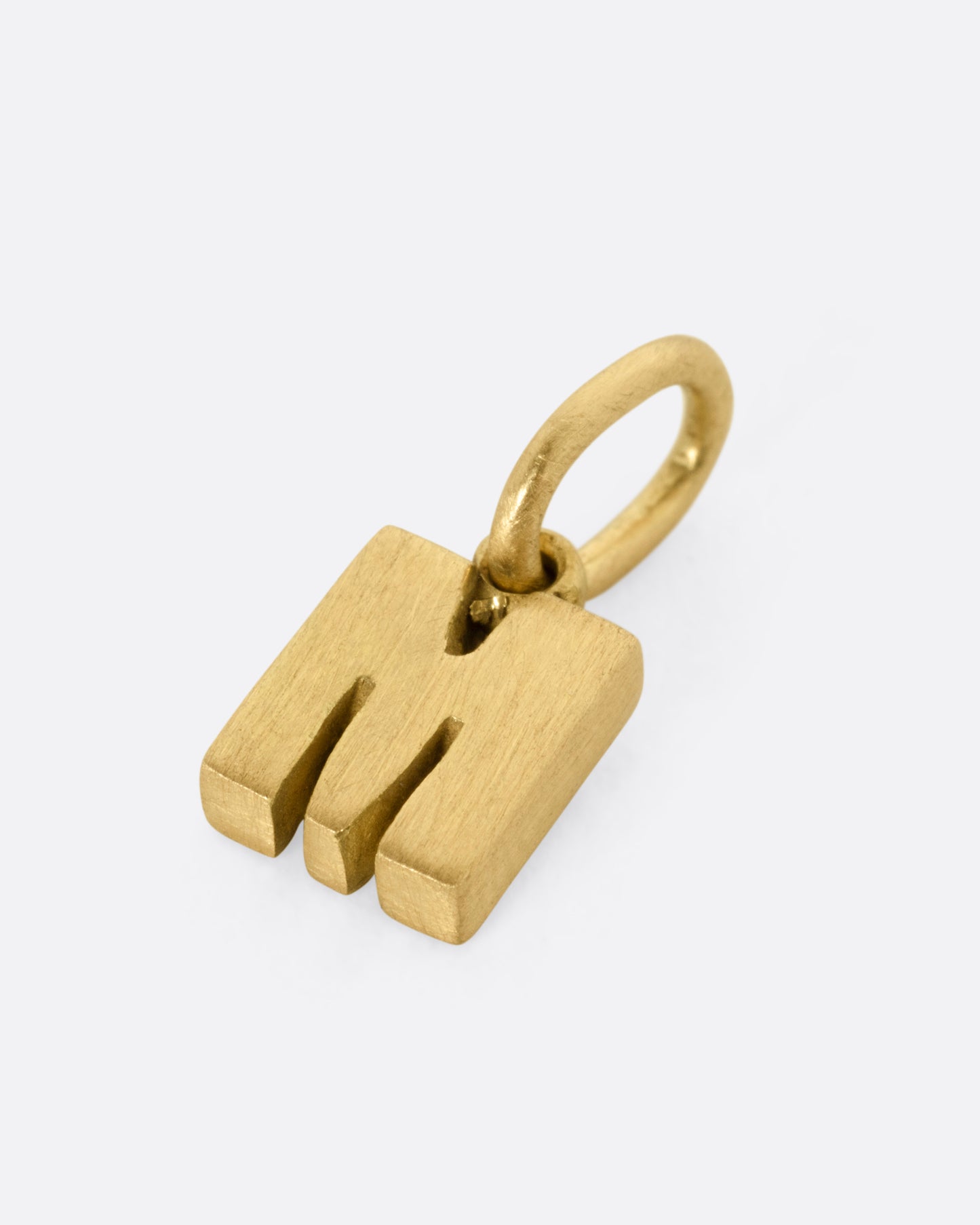 A yellow gold letter 'M' pendant shown from the side.