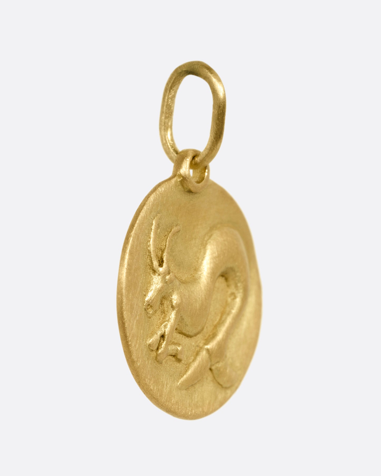 A circular yellow gold Capricorn pendant with a sea goat, shown from the side.