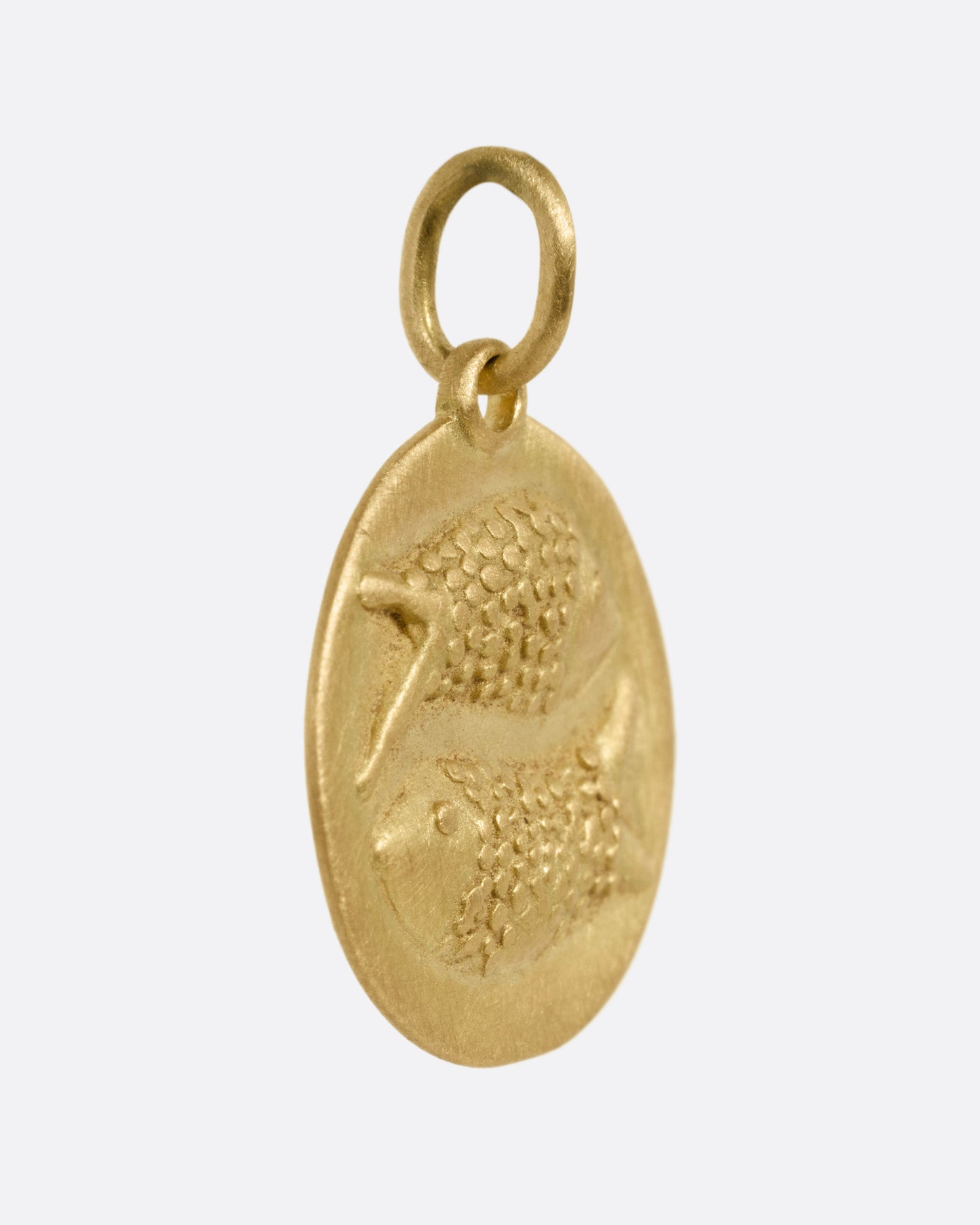 A circular yellow gold Pisces pendant with two fish on its front, shown from the side.
