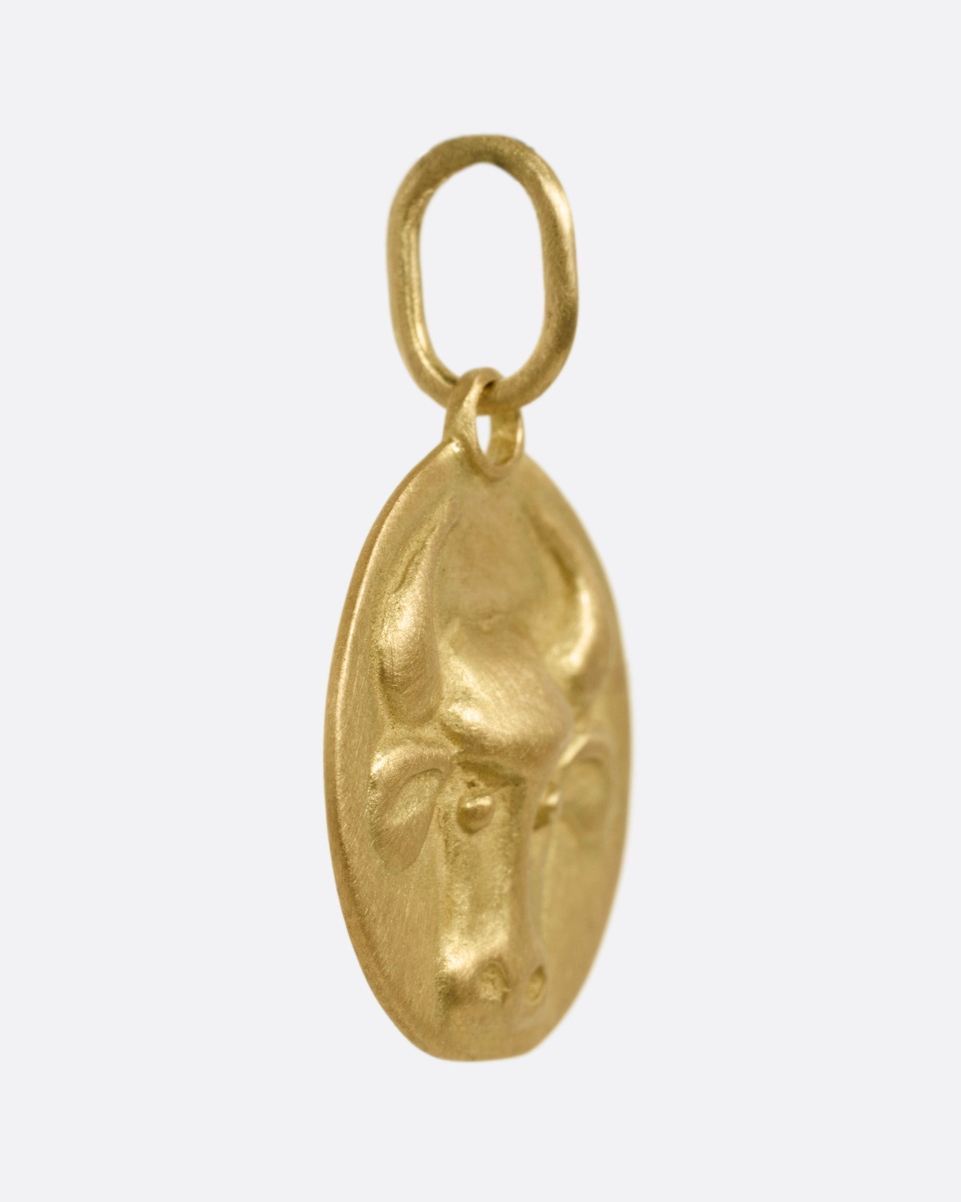 A circular yellow gold Taurus pendant with a bull head, shown from the side.