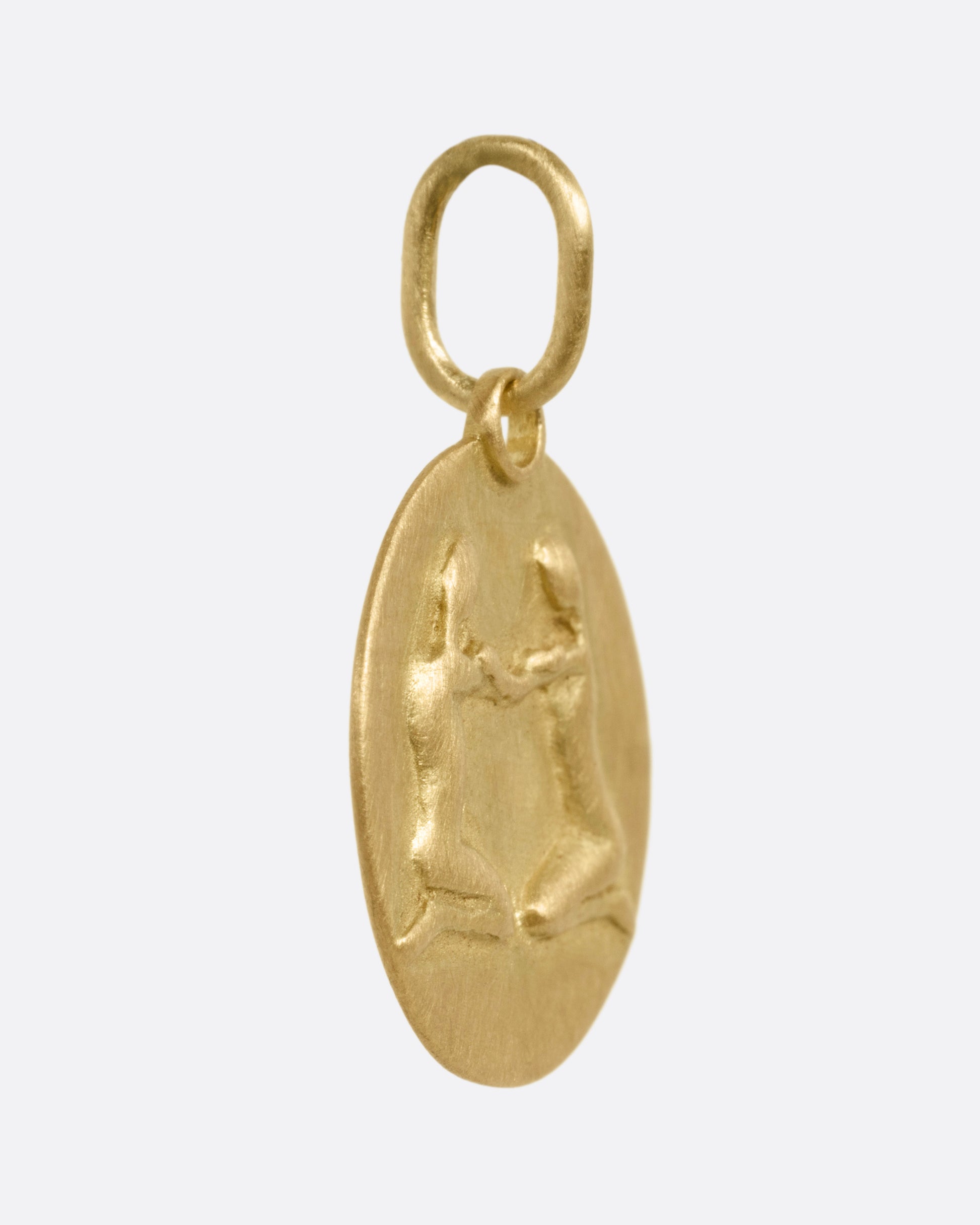 A circular yellow gold Gemini pendant with the twins, shown from the side.