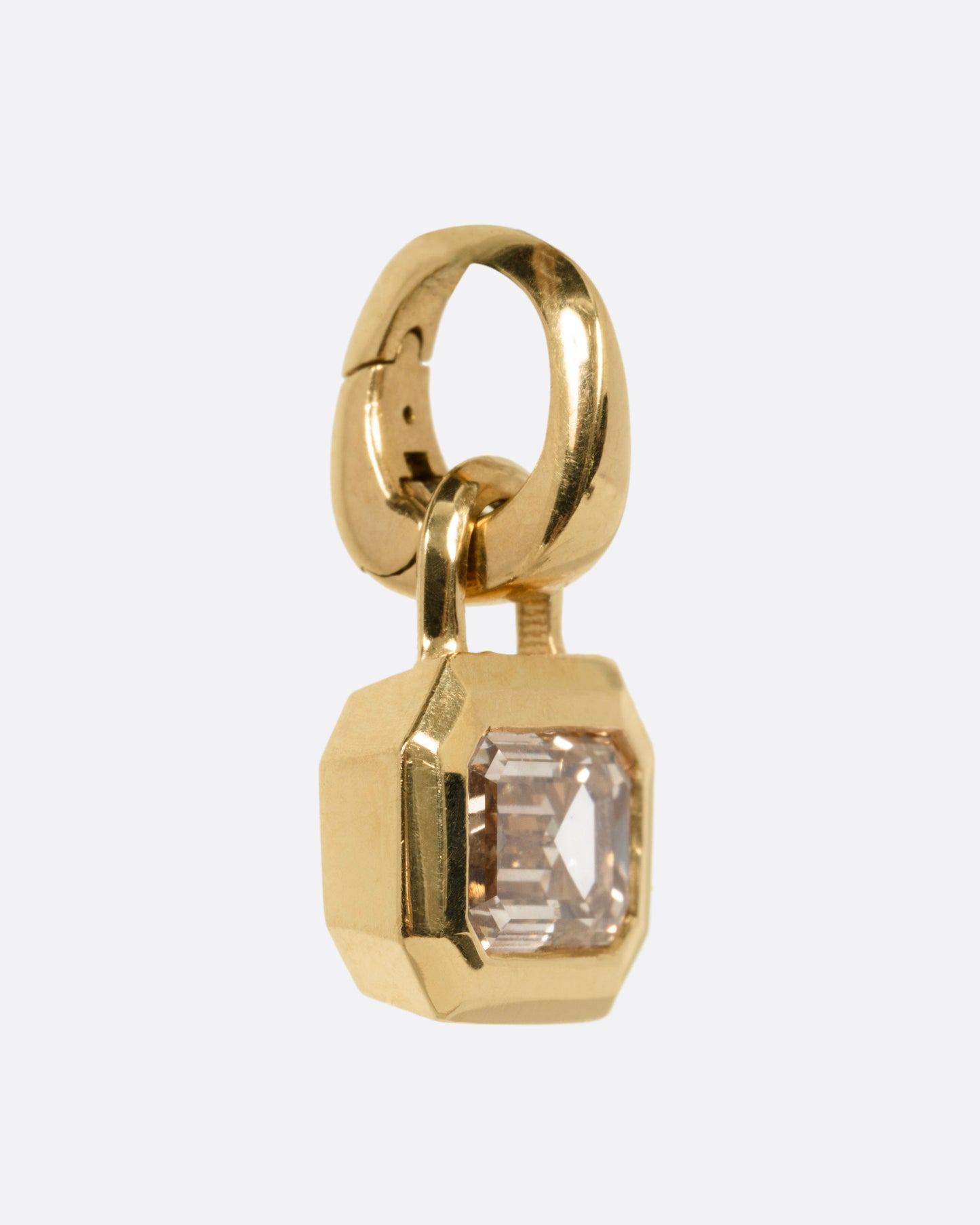 A yellow gold charm with a step cut champagne diamond, shown from the side.