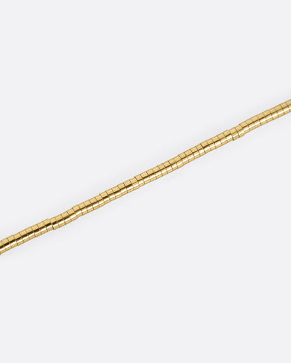 A close up of a yellow gold chain necklace with a queue of cylindrical gold beads.