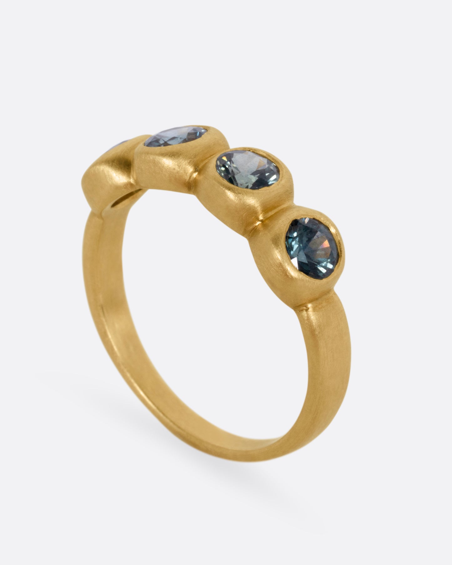 A yellow gold ring with four bezel set green sapphires, shown standing up from the side.
