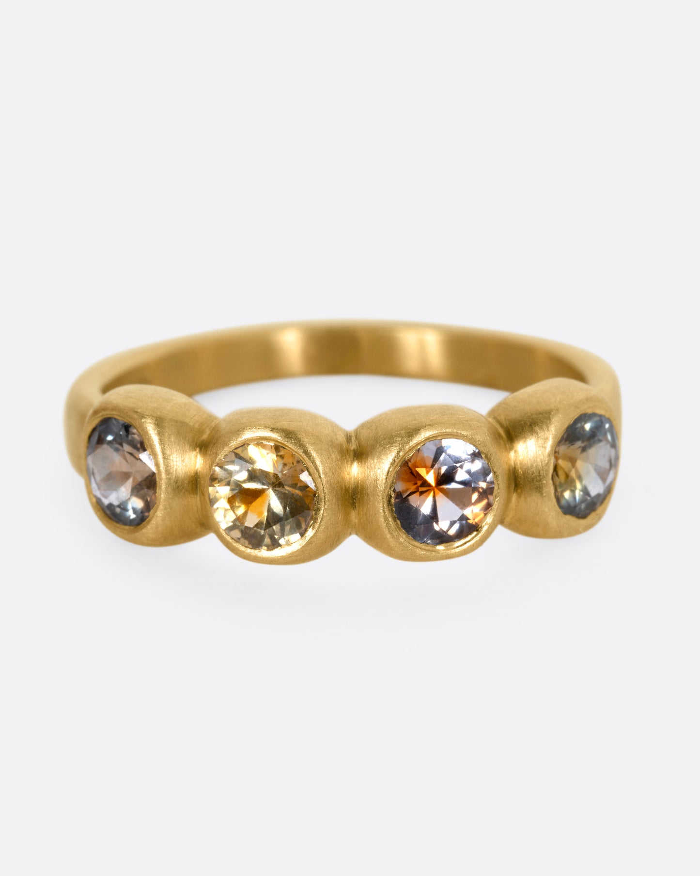 A yellow gold ring with four bezel set kaleidoscope sapphires, shown from the front.