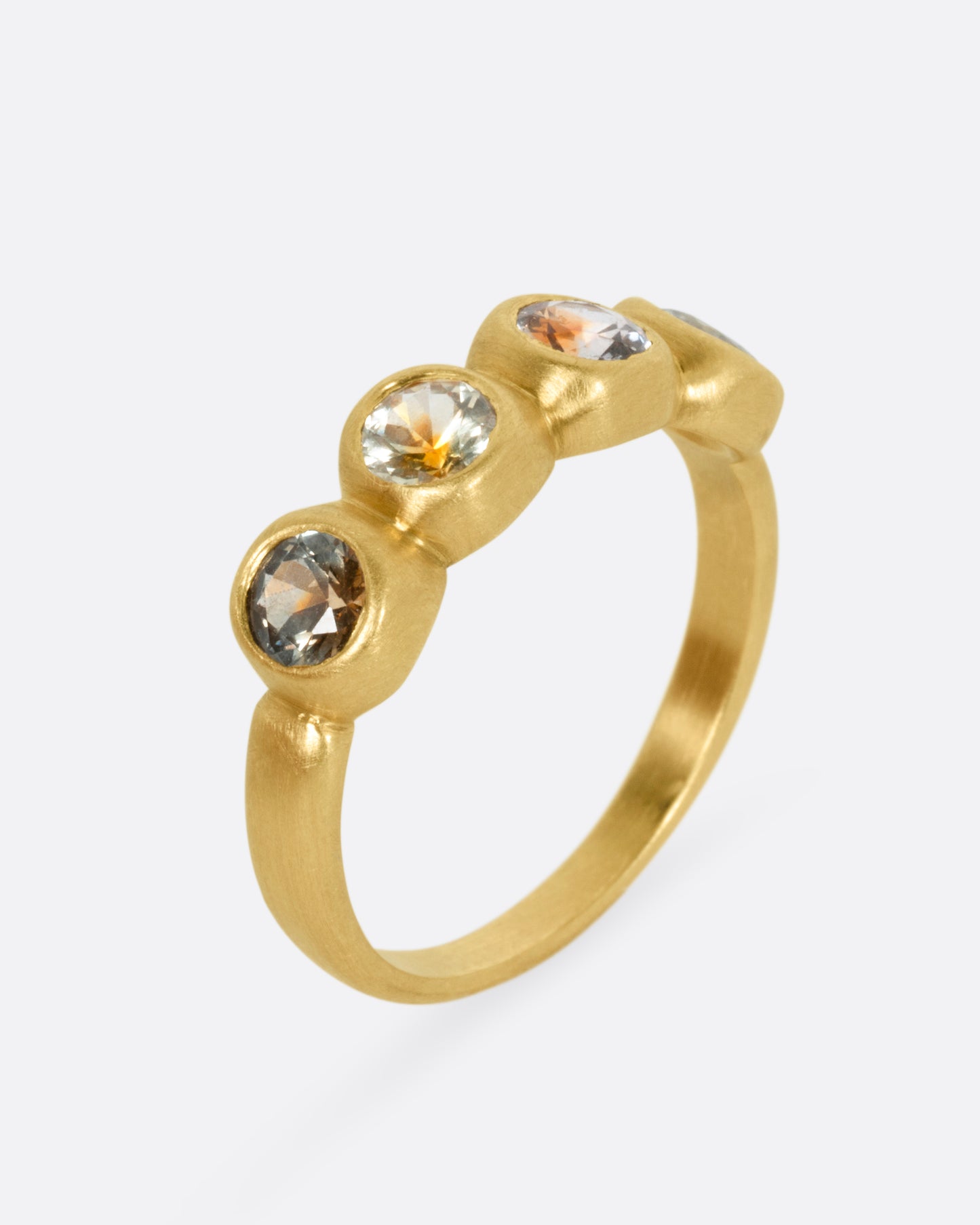A yellow gold ring with four bezel set kaleidoscope sapphires, shown from the side standing up.