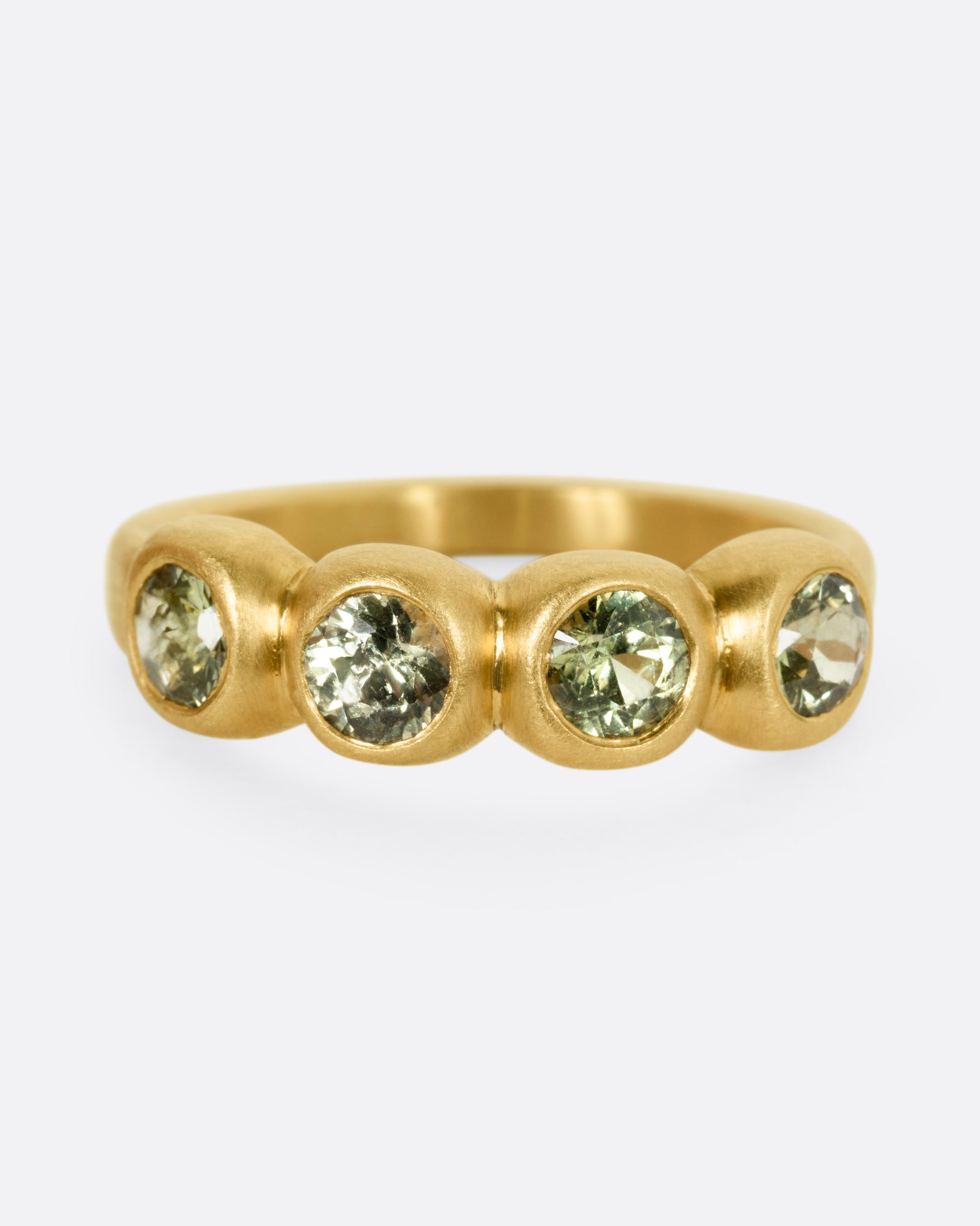 A yellow gold ring with four bezel set green sapphires, shown from the front.