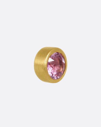 A yellow gold stud earring with a pink sapphire, shown from the side.