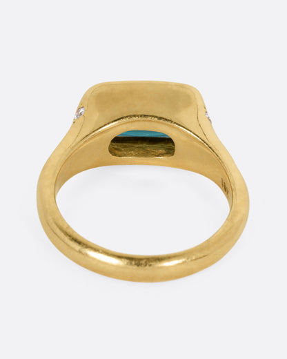 A yellow gold ring with a rectangular green tourmaline at the center and diamonds on either shoulder. Shown from the back.