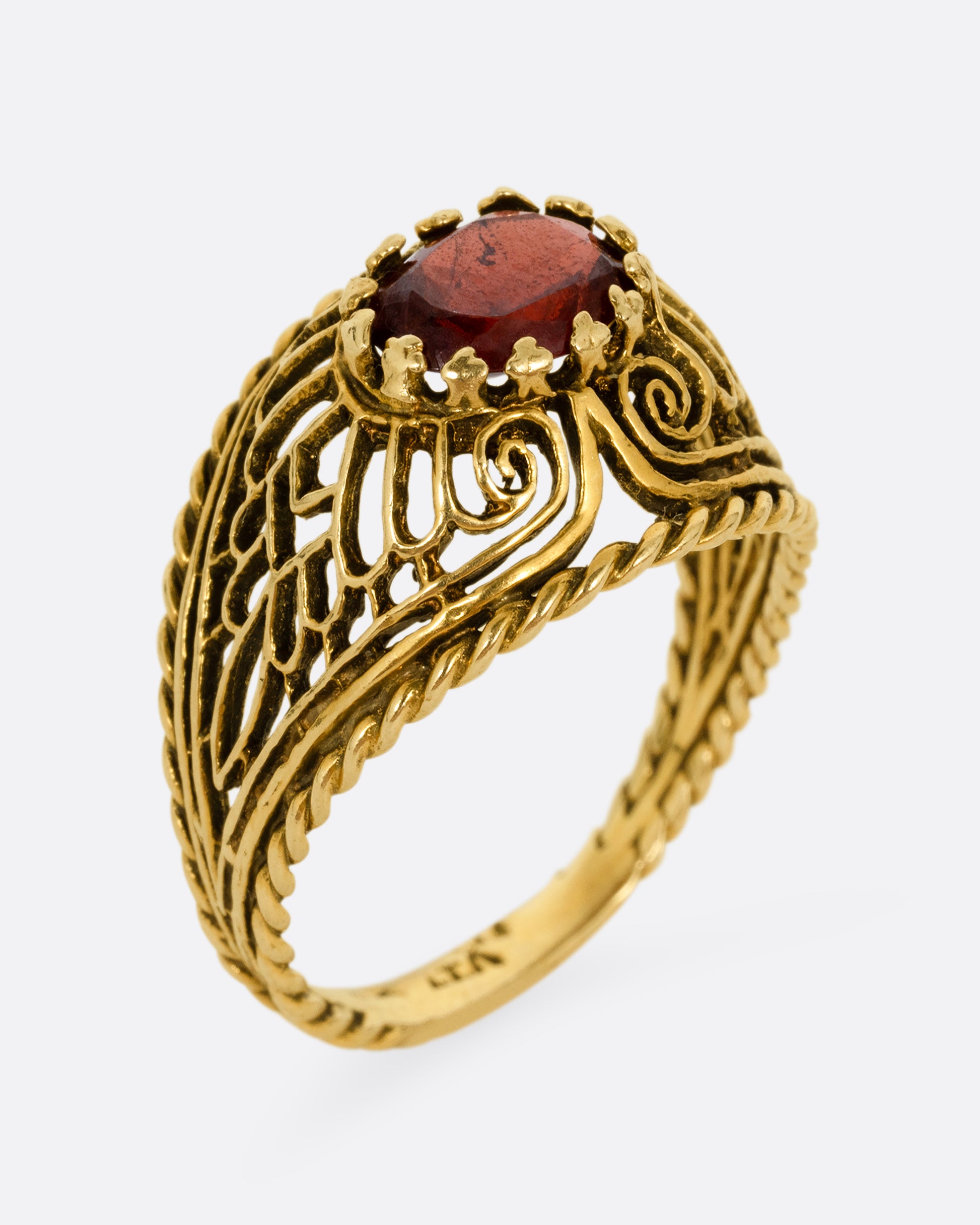 A yellow gold dome ring with an intricate web of filigree and delicate cutouts and a garnet at its center. Shown from the side standing up.