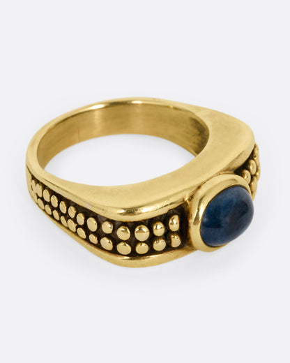 A yellow gold ring with a sapphire and raised circular pattern along the band, shown from the side.