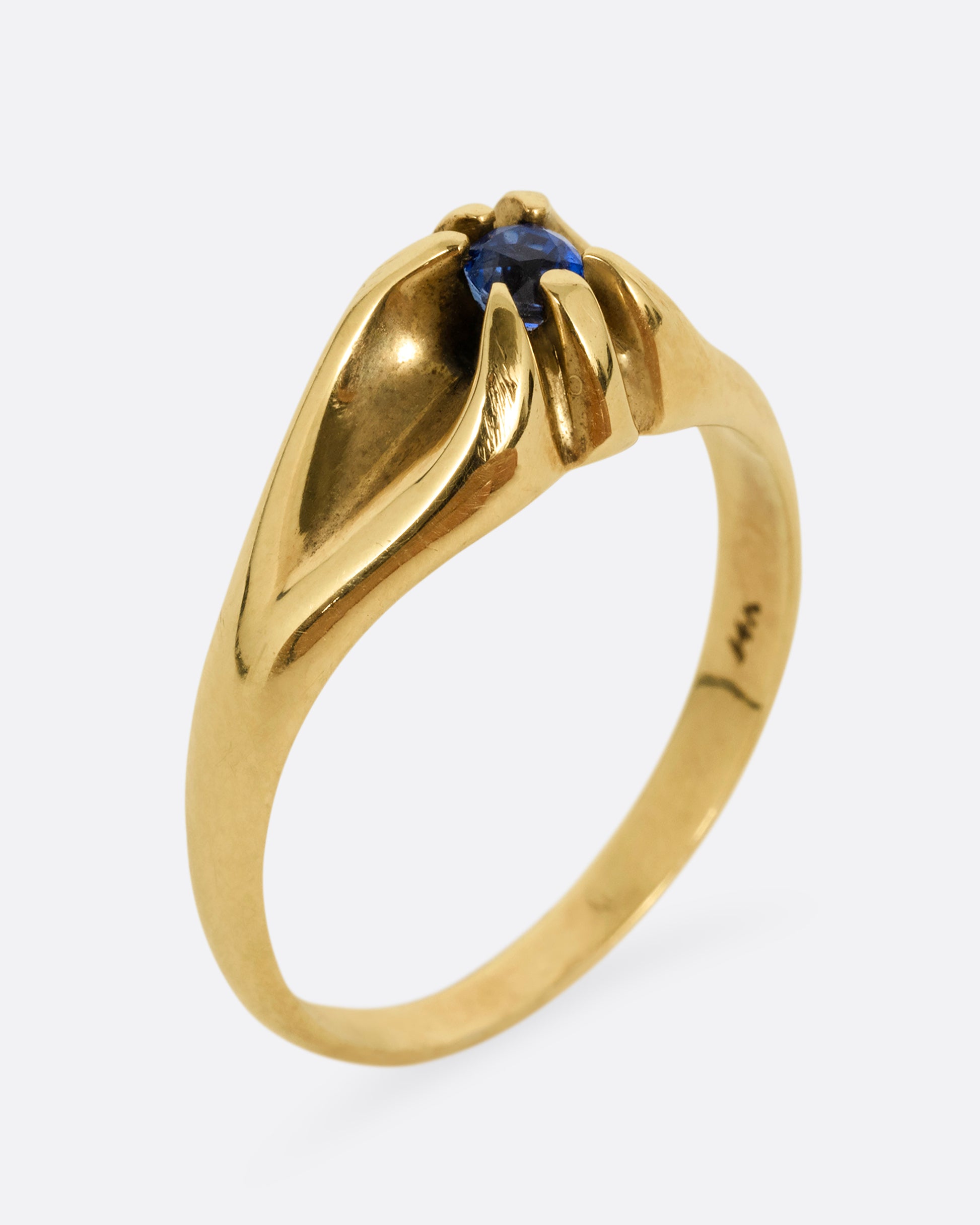 A yellow gold ring with a prong set blue sapphire. Shown standing up from the front.