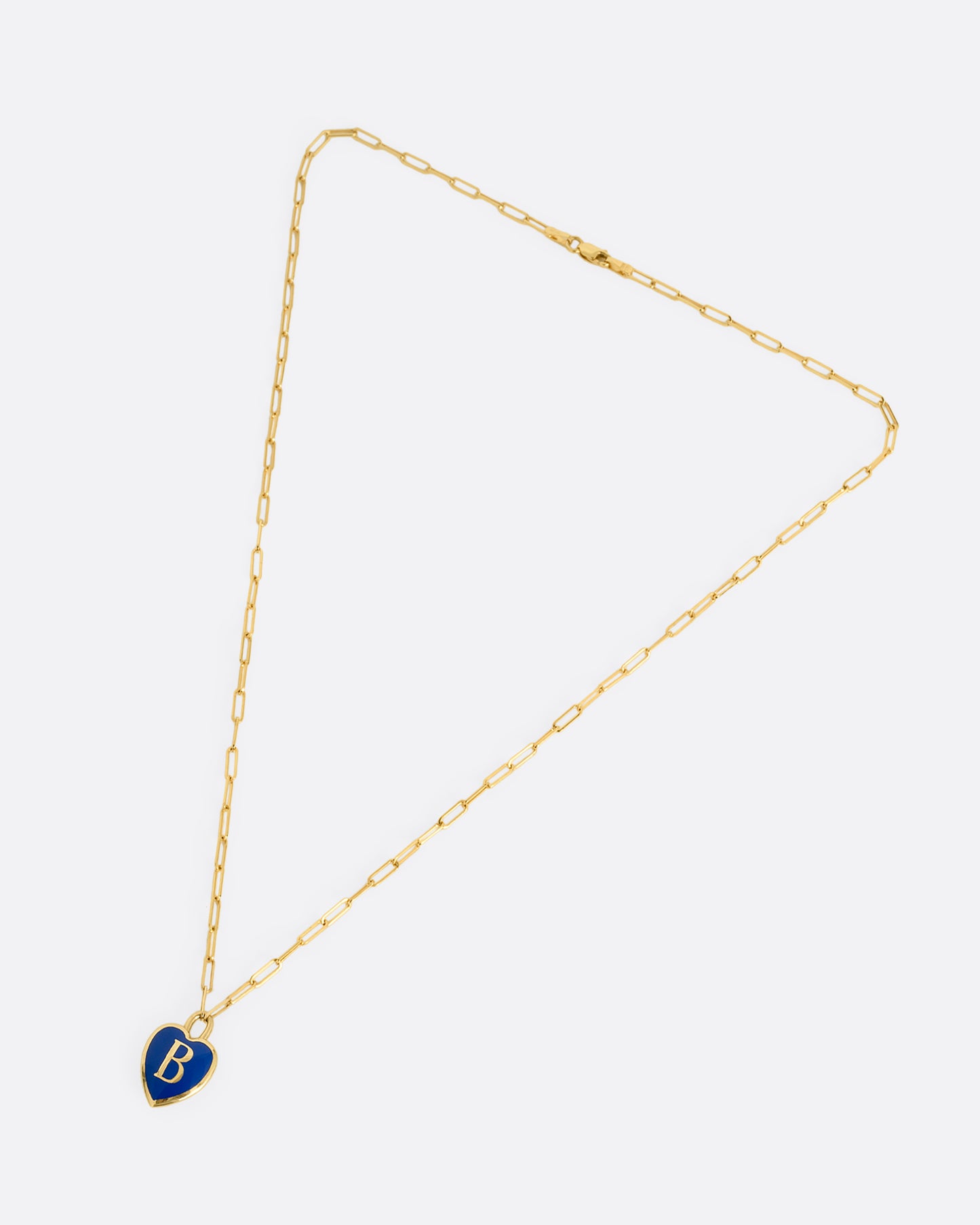 A yellow gold  paperclip chain necklace with a black enamel heart shaped N pendant. Shown closed lying flat at an angle from the front.
