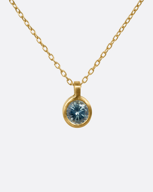 A yellow gold cable chain necklace with a round bezel set faceted blue green sapphire. Shown from the front.