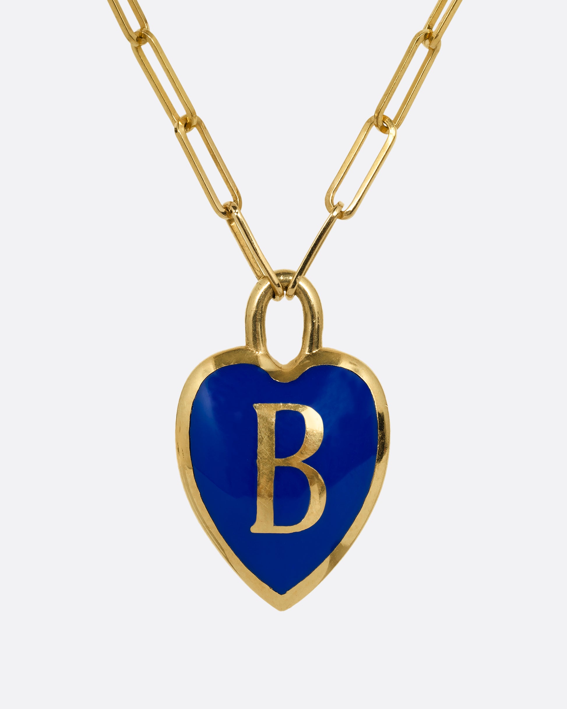 A yellow gold  paperclip chain necklace with a blue enamel heart shaped B pendant. Shown from the front.
