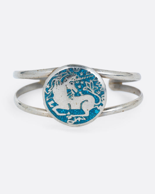 An alpaca silver cuff bracelet with a circular face with a unicorn in turquoise inlay. Shown from the front.