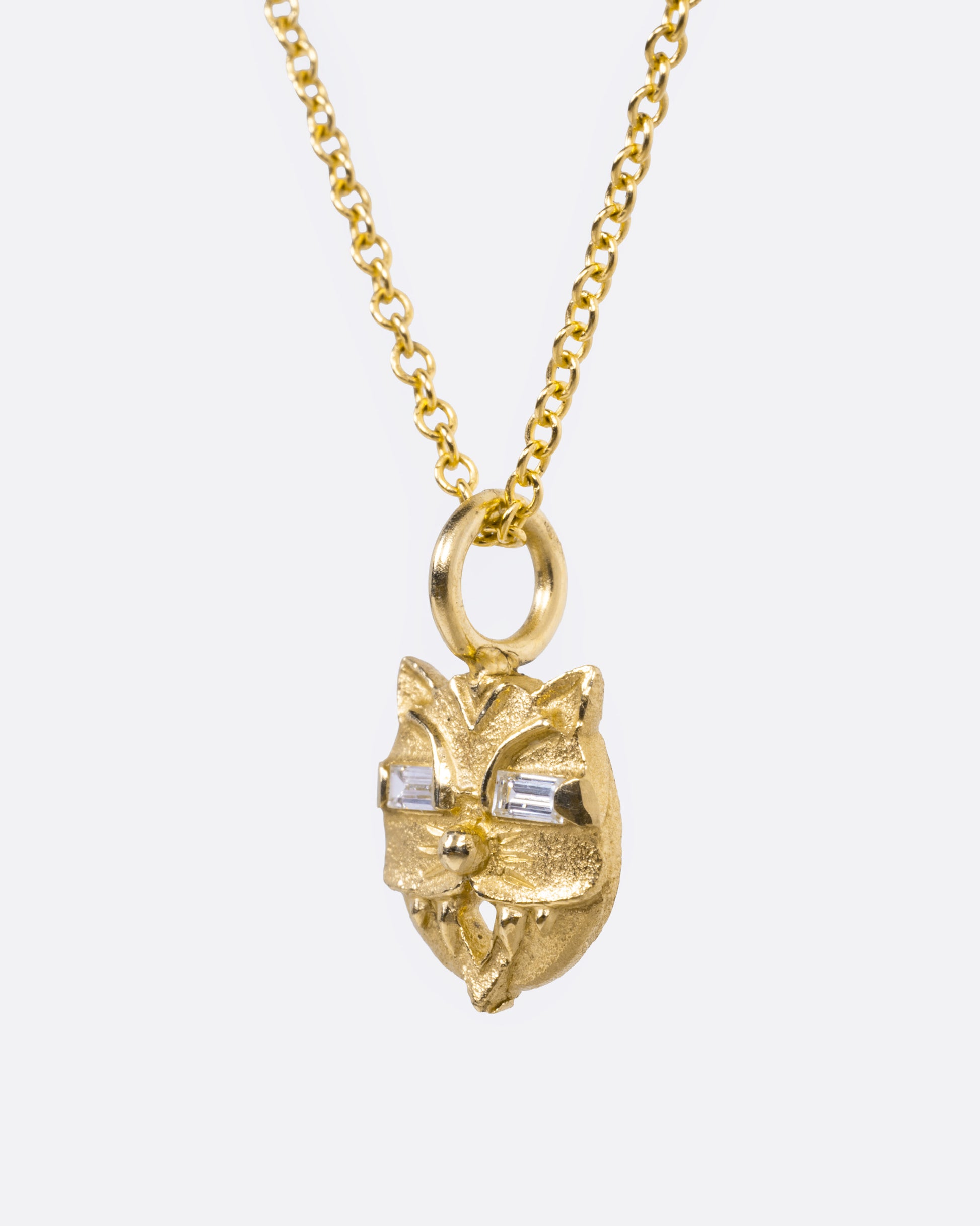 A yellow gold cable chain necklace with a cat head shaped pendant with baguette diamond eyes, shown from the side.