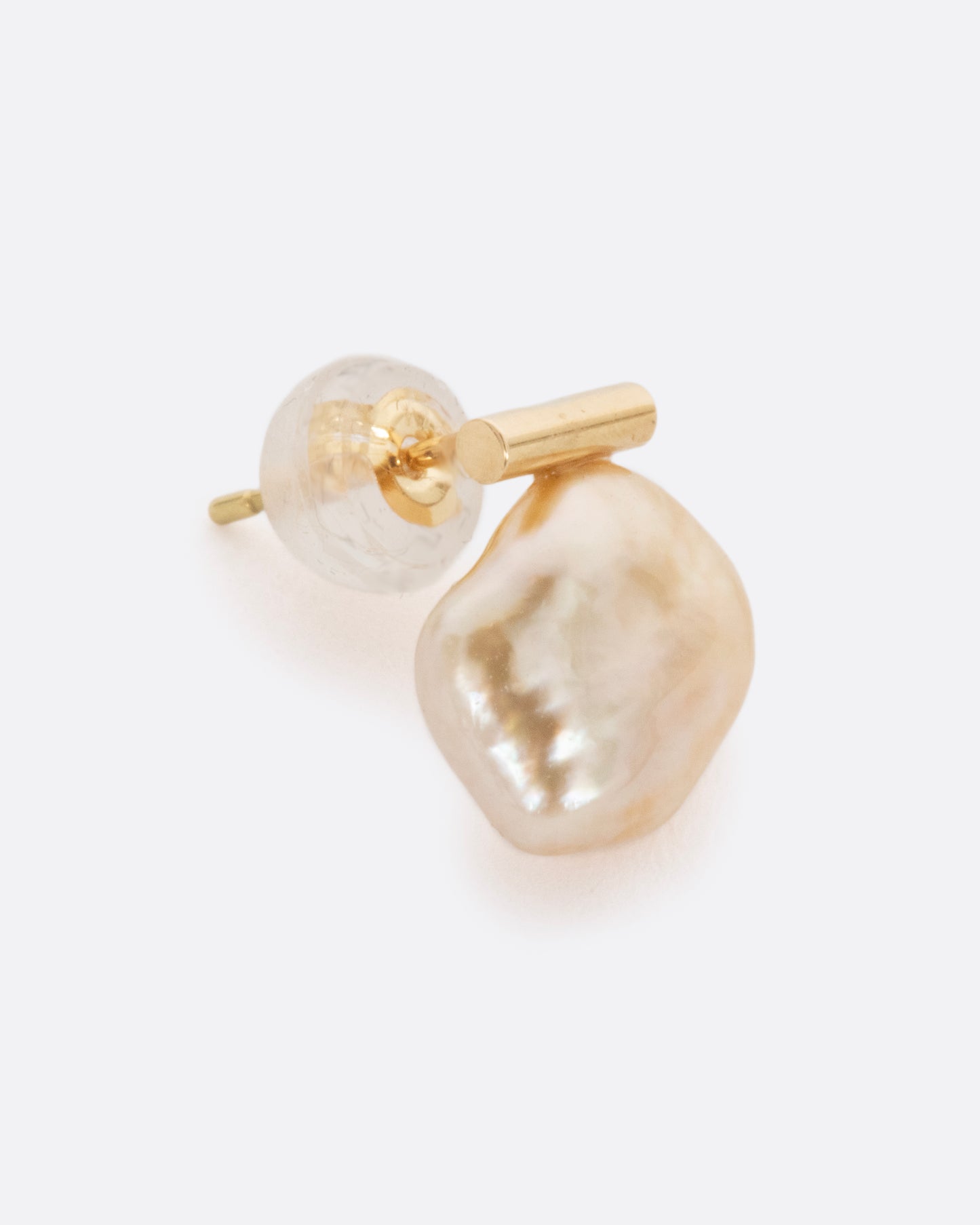 A freeform South Sea baroque pearl is suspended from a modern gold bar setting. The organic curvature of this rare pearl allows light to reflect in all directions, creating radiance from every angle... A sleek yet natural piece. View from the side.