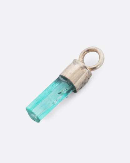 A Colombian emerald dangle in a yellow gold bail. Shown diagonally lying flat from the front.