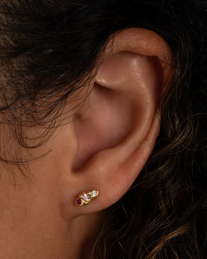 Yellow gold pink and red sapphire stud earrings worn on an ear
