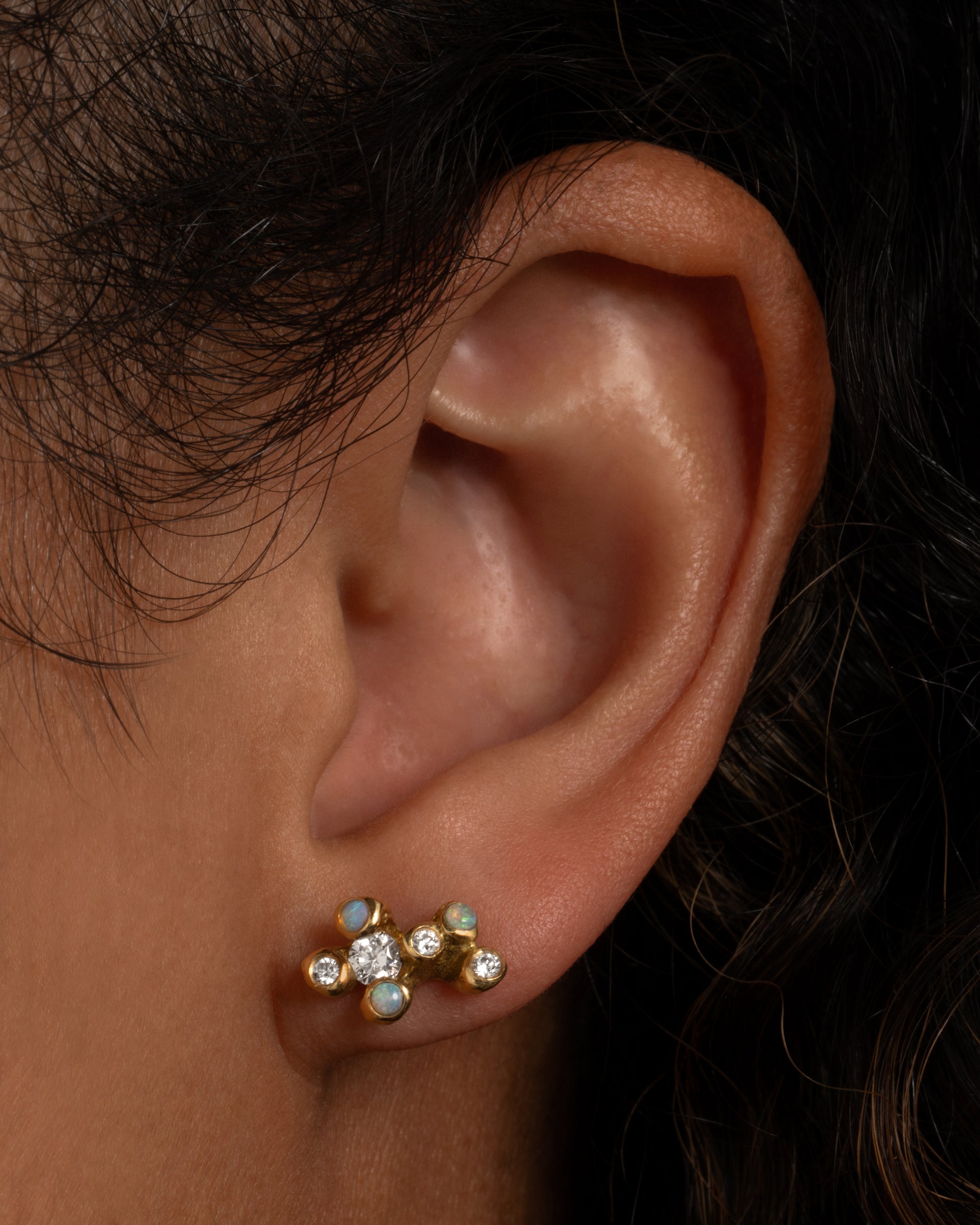 A yellow gold stud earring with a cluster of diamonds and opals. Shown from the front on a person.