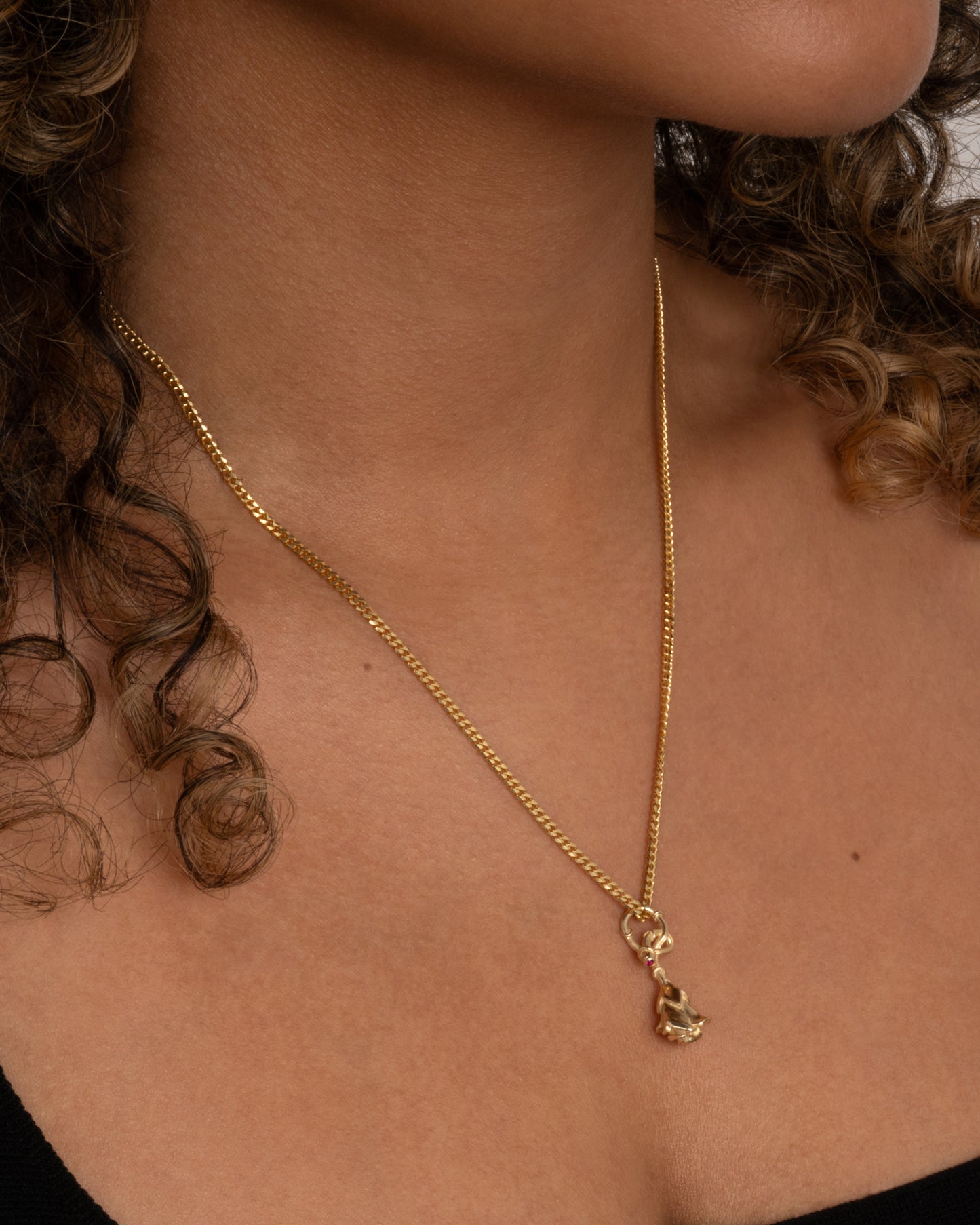 yellow gold rose charm with ruby, shown worn on a chain around the neck