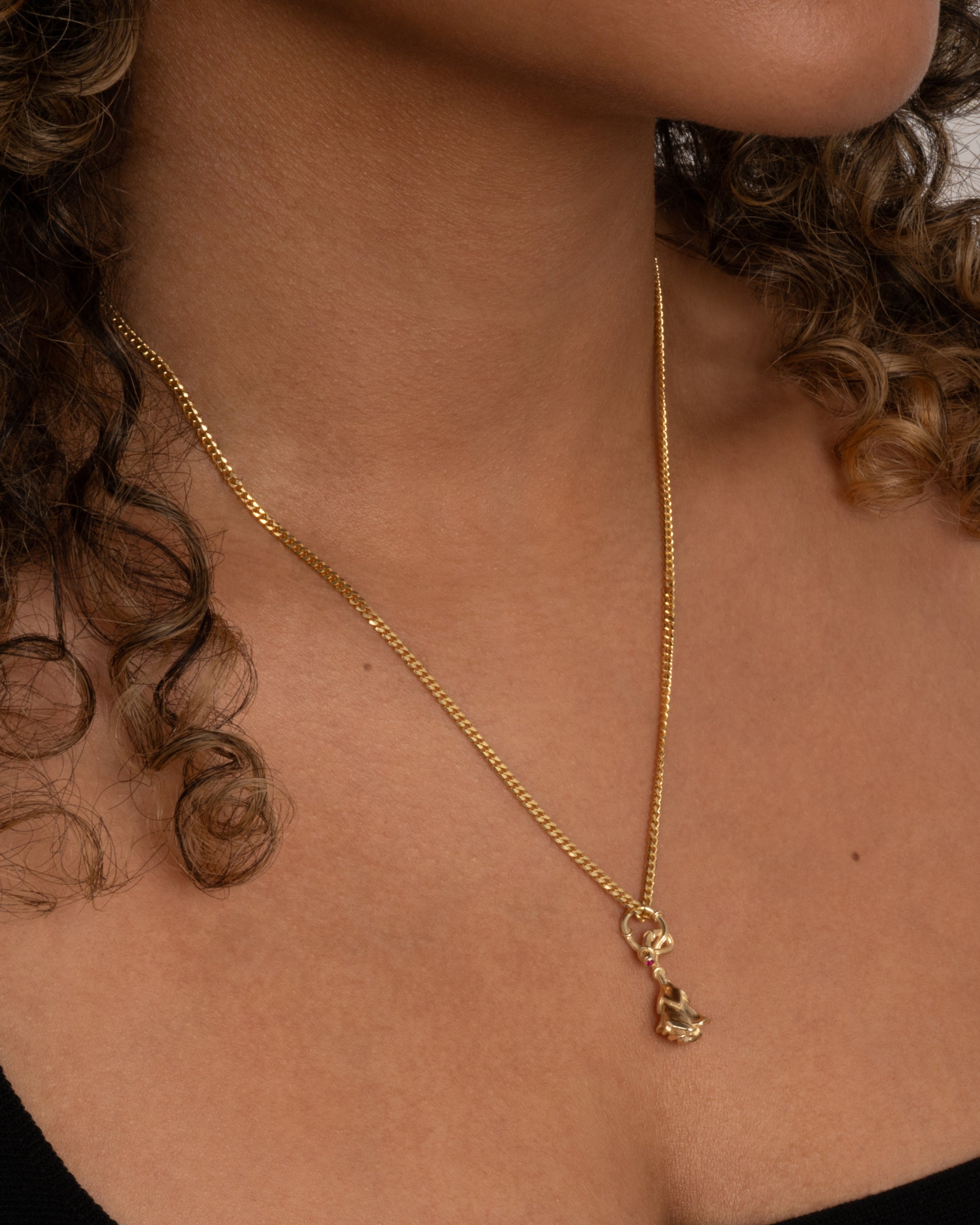 yellow gold rose charm with ruby, shown worn on a chain around the neck