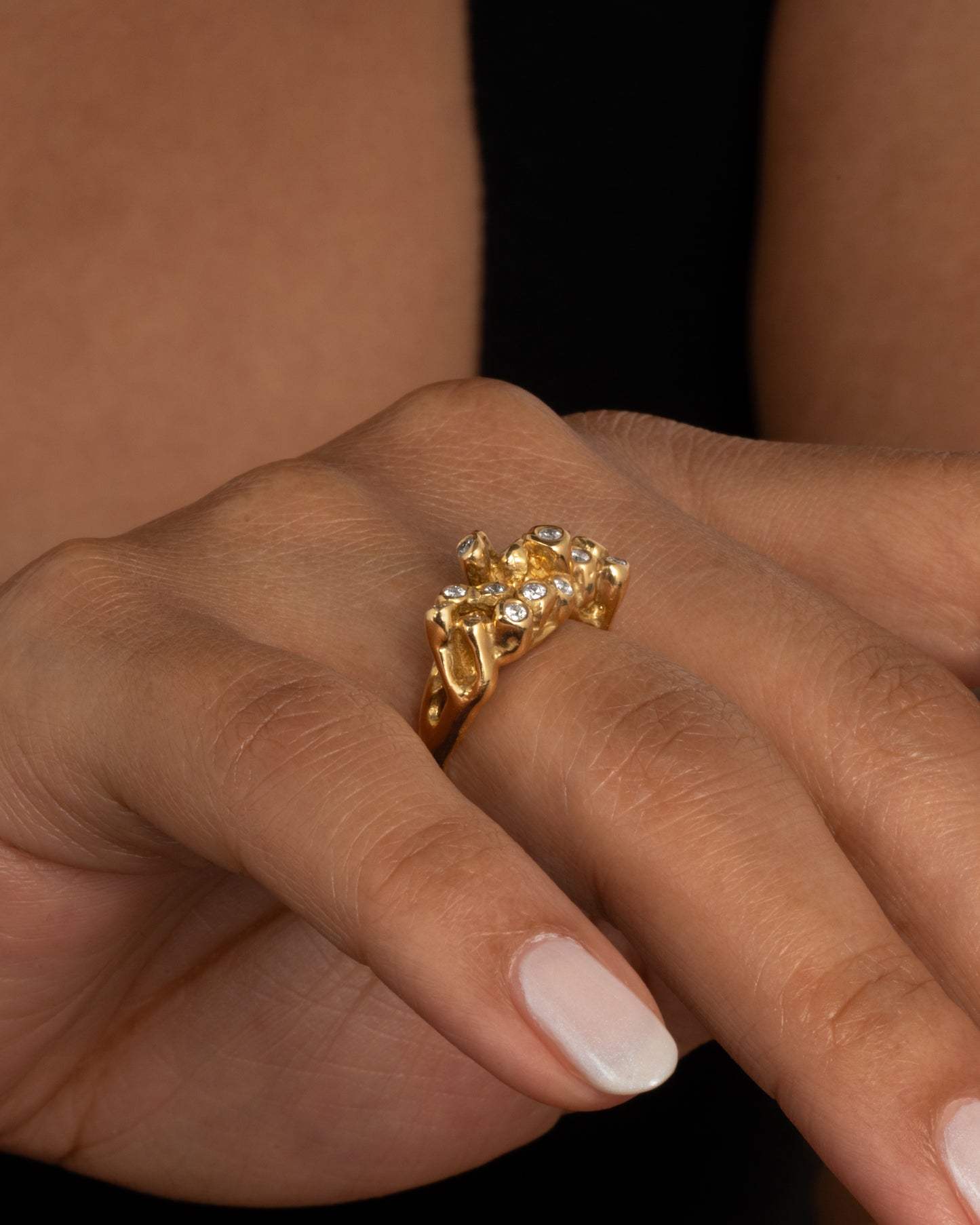 A yellow gold ring with sea anemone tentacles, dotted with diamonds, shown worn on a finger.
