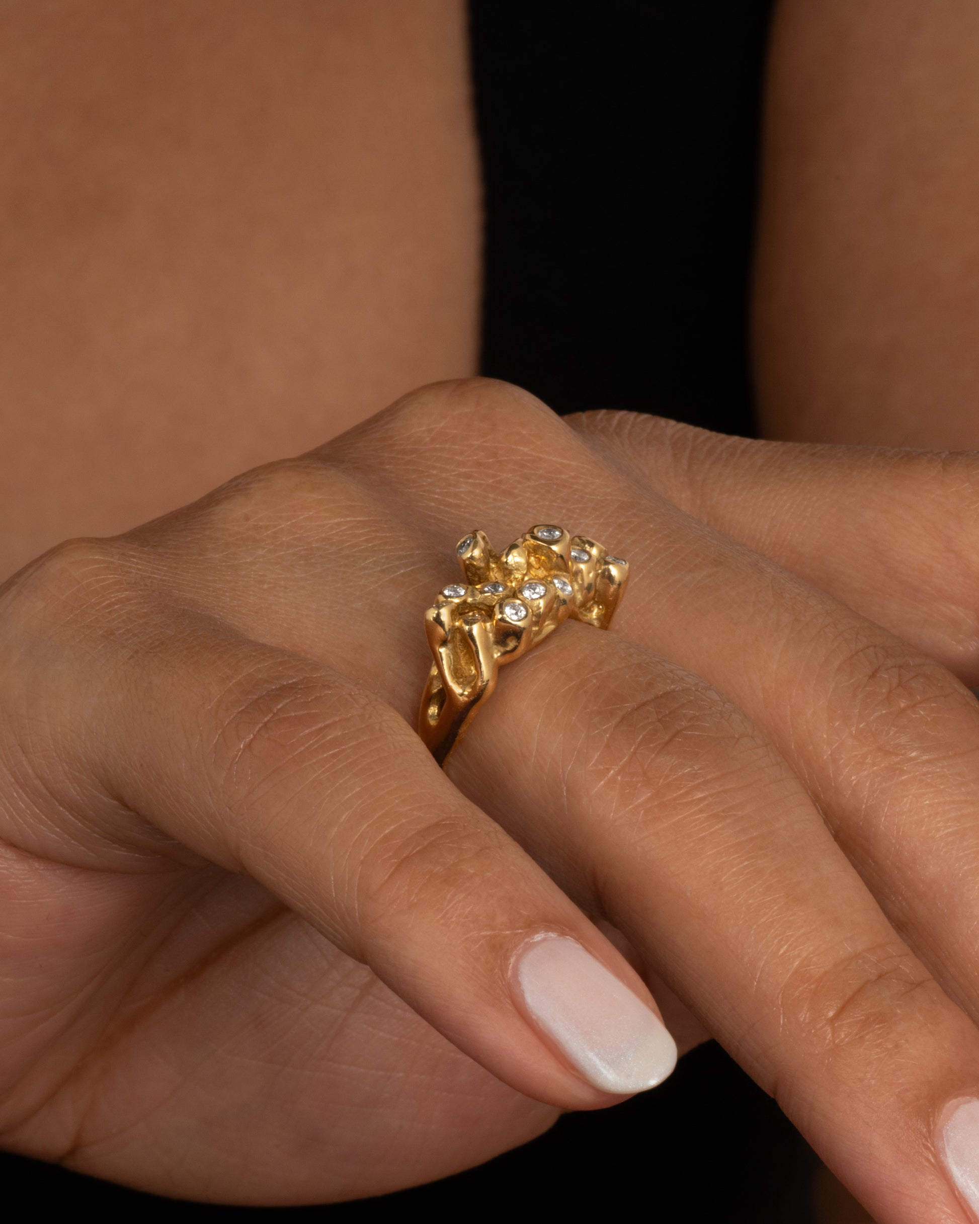 A yellow gold ring with sea anemone tentacles, dotted with diamonds, shown worn on a finger.