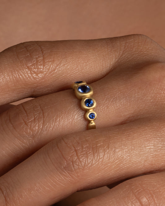 A yellow gold ring with blue sapphires, shown on a hand.