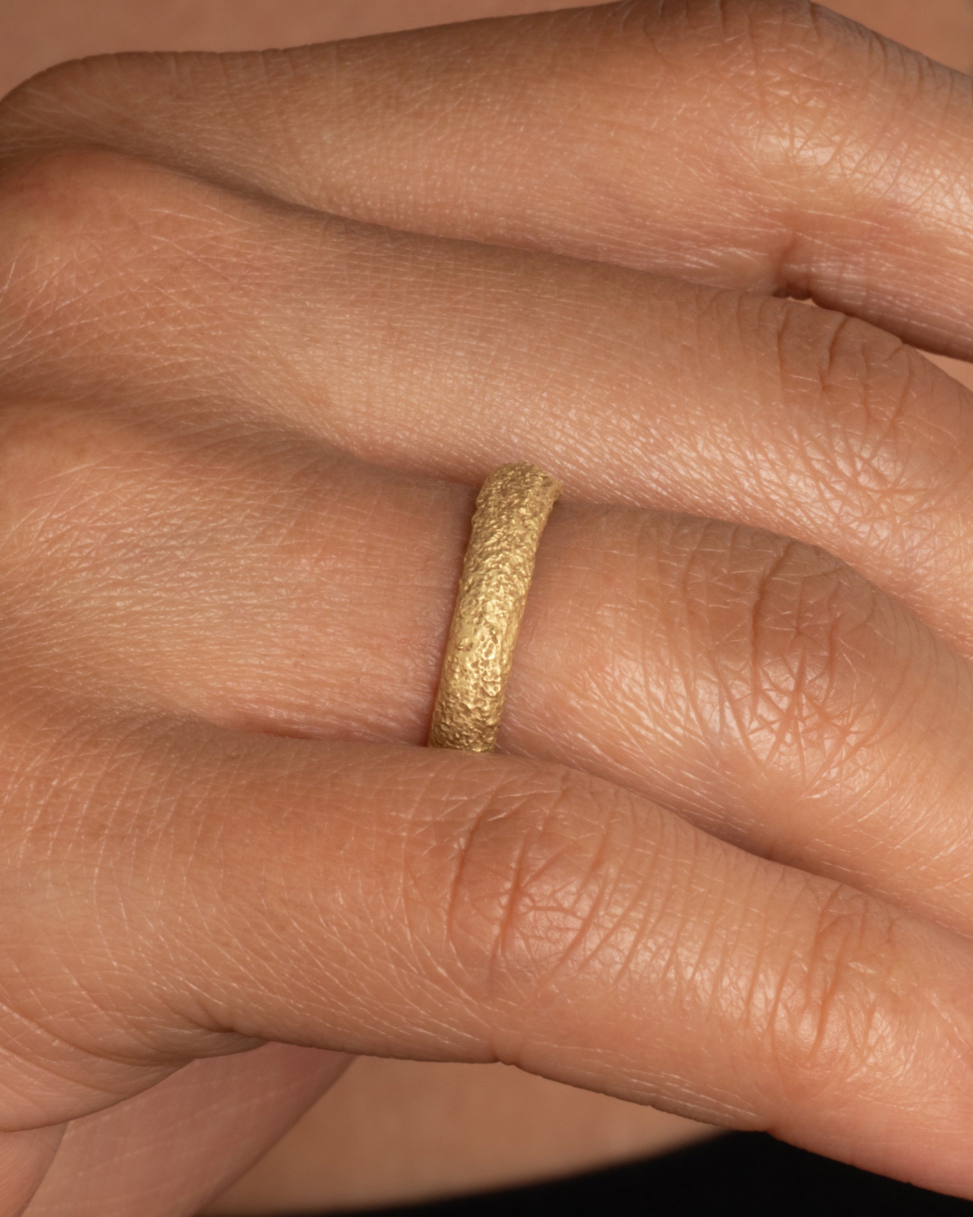 A textured yellow gold band. Shown on a finger.