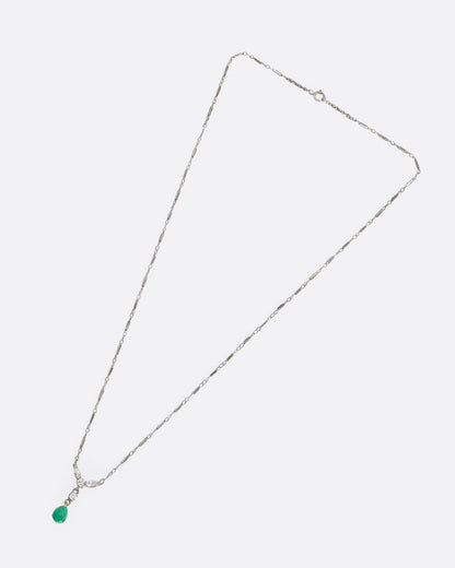 White gold necklace featuring diamonds and an emerald at the center. View from above, lying flat.