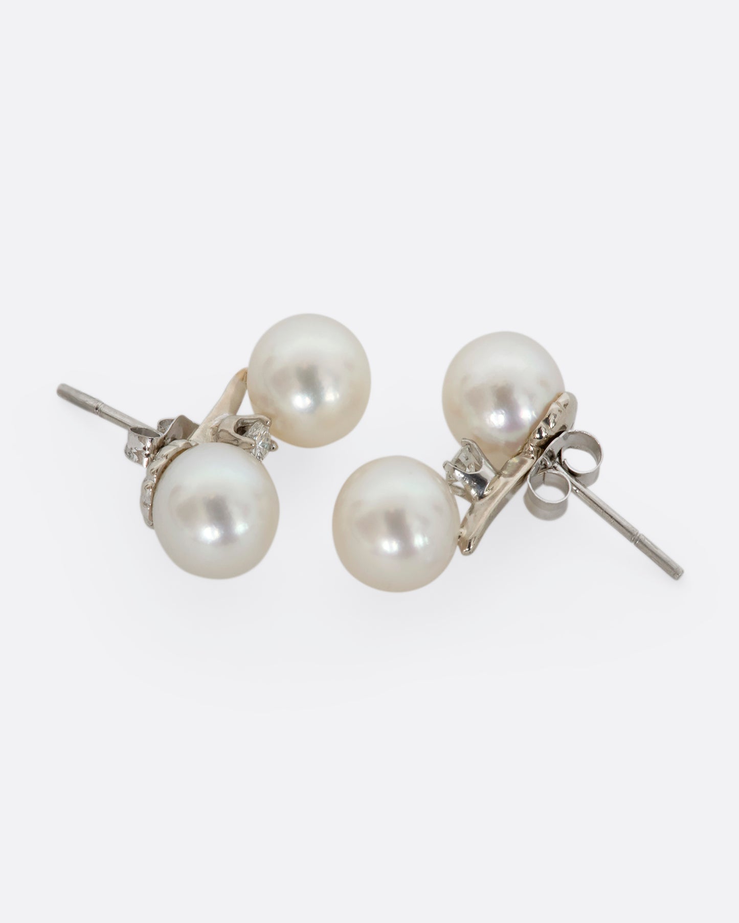 A pair of white gold studs featuring two pearls with a diamond situated in between. View from the front and back alternating.