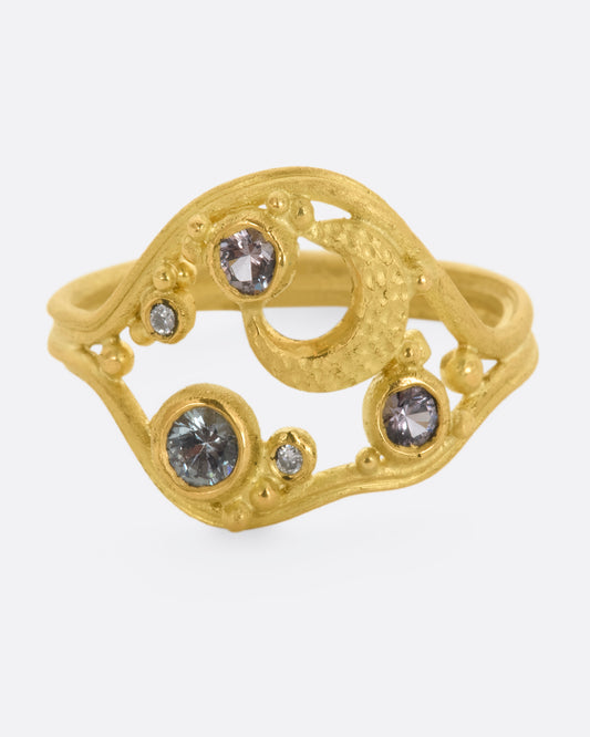 A yellow gold ring featuring a crescent moon, pink and purple spinels and diamonds within a gold frame. View from the front.