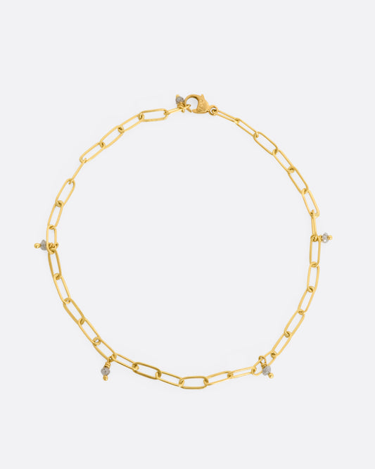 A yellow gold oval link bracelet with 5 tiny raw diamond beads spaced throughout. View lying flat, from above.