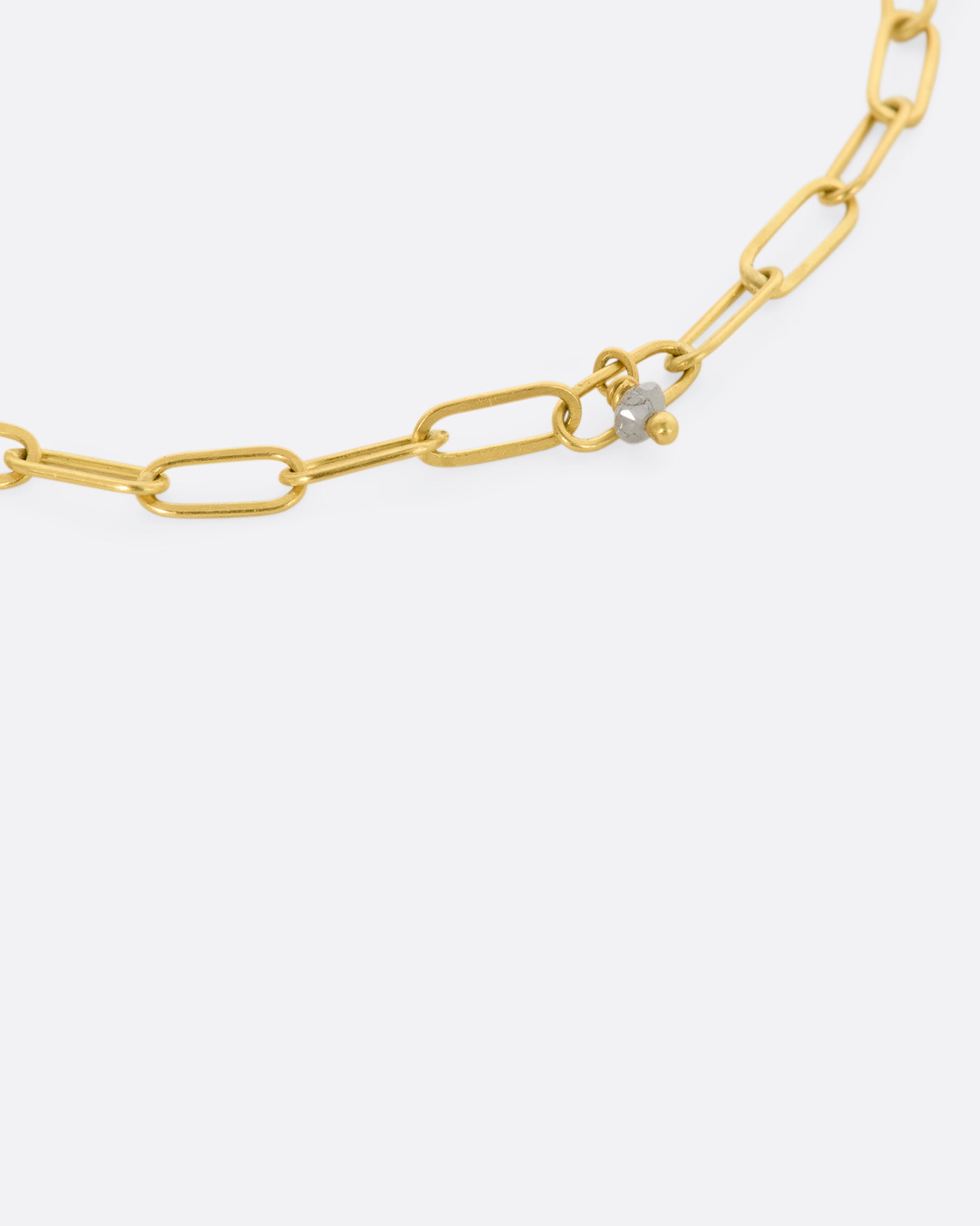 A yellow gold oval link bracelet with 5 tiny raw diamond beads spaced throughout. Close up view of single raw diamond and chain links. 