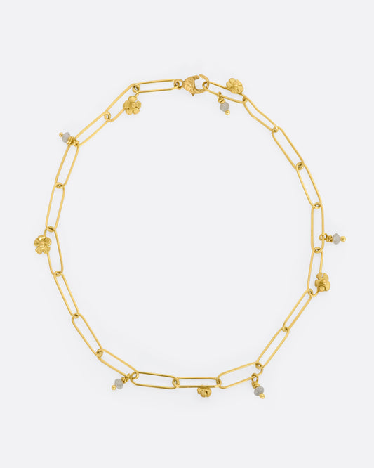 A yellow gold oval link bracelet with tiny raw diamond beads and flowers spaced throughout. View lying flat, from above.
