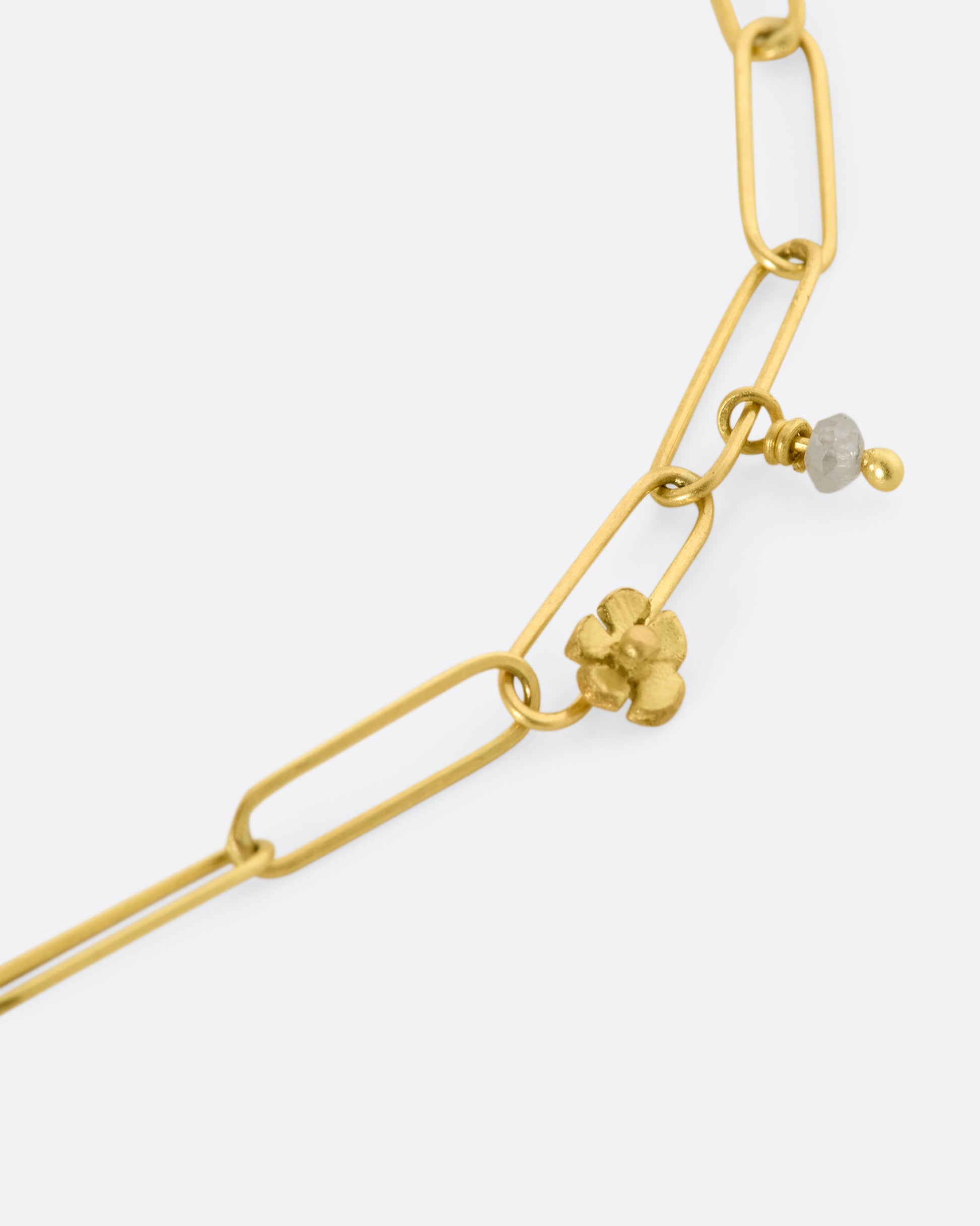 A yellow gold oval link bracelet with tiny raw diamond beads and flowers spaced throughout. Close up view of single raw diamond, flower and chain links.