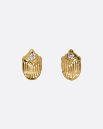 A pair of yellow gold scarab shaped stud earrings, each punctuated by a diamond, shown from the front.