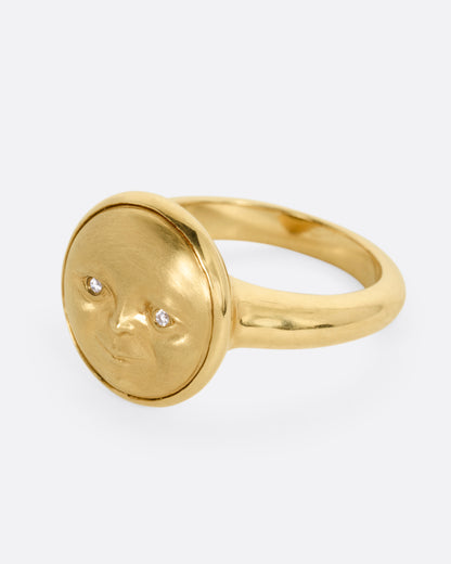 A yellow gold ring with a moon face and diamond eyes. Shown from the side.