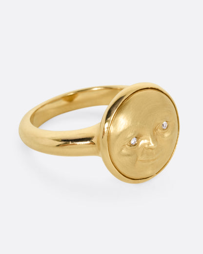 A yellow gold ring with a moon face and diamond eyes. Shown from the side.