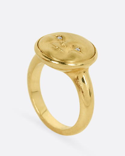A yellow gold ring with a moon face and diamond eyes. Shown from the side standing up.