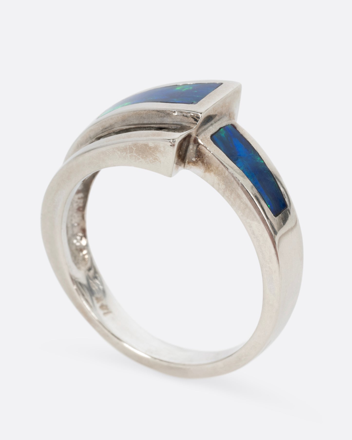 A white gold wrap ring with opal inlay and  a queue of diamonds along the edge, shown standing up from the side.