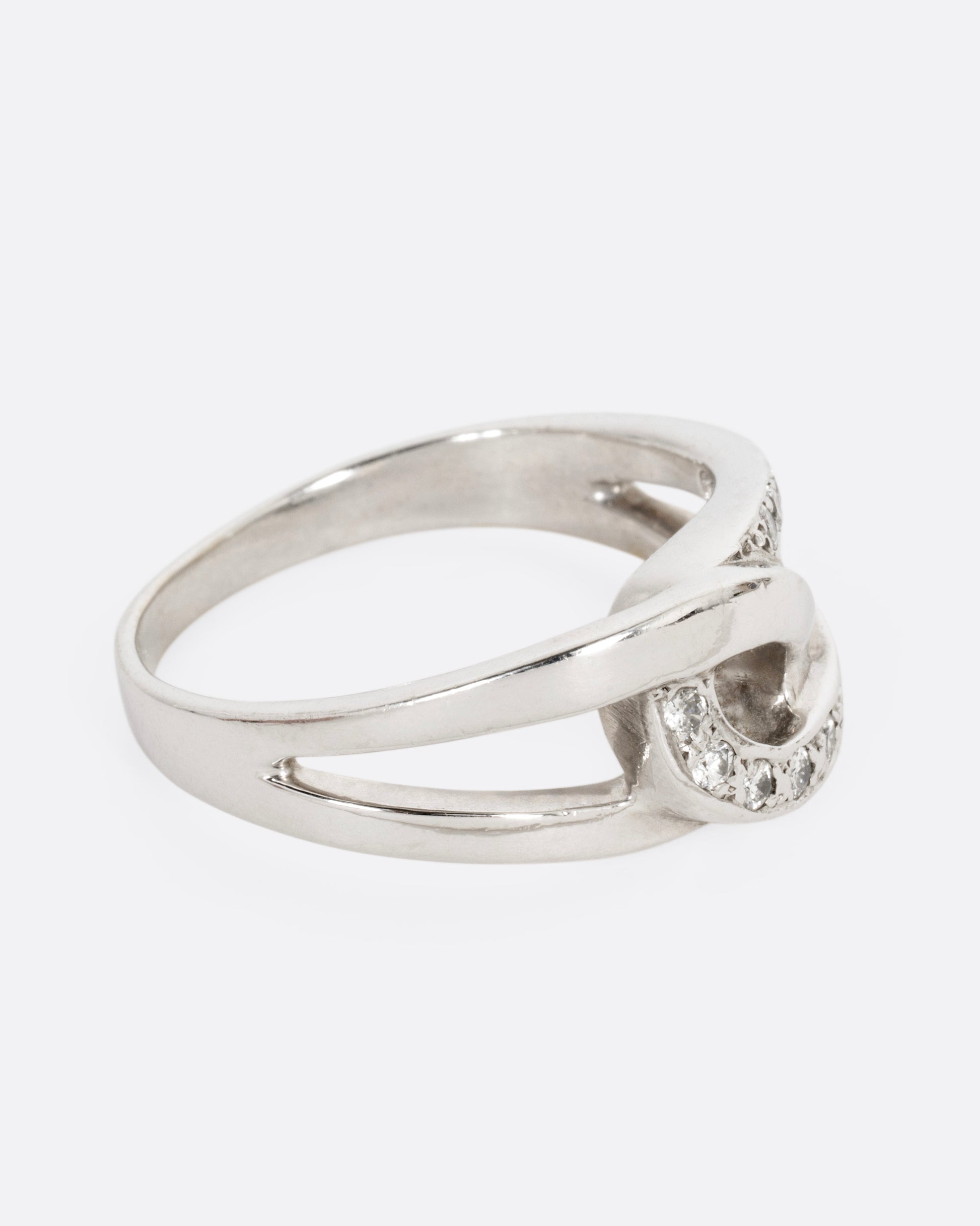 A white gold ring with two interlocking loops; one studded with diamonds, shown from the side.