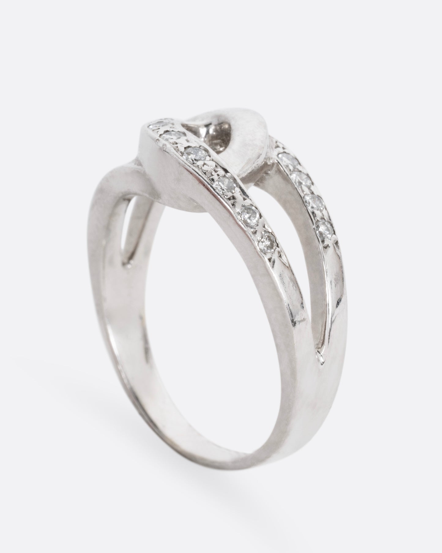 A white gold ring with two interlocking loops; one studded with diamonds, shown from the side standing up.