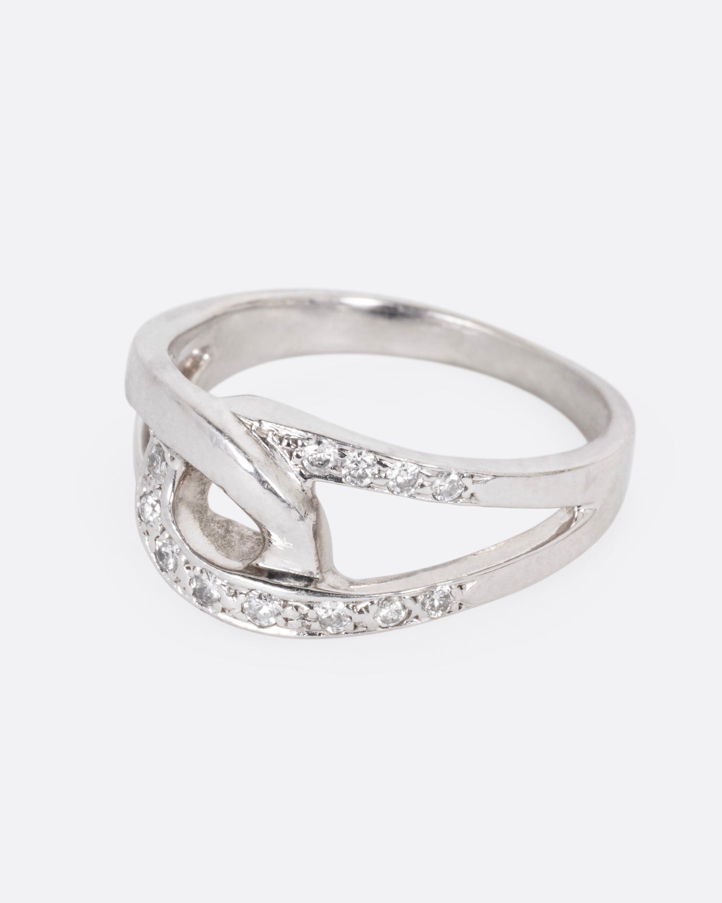 A white gold ring with two interlocking loops; one studded with diamonds, shown from the side.