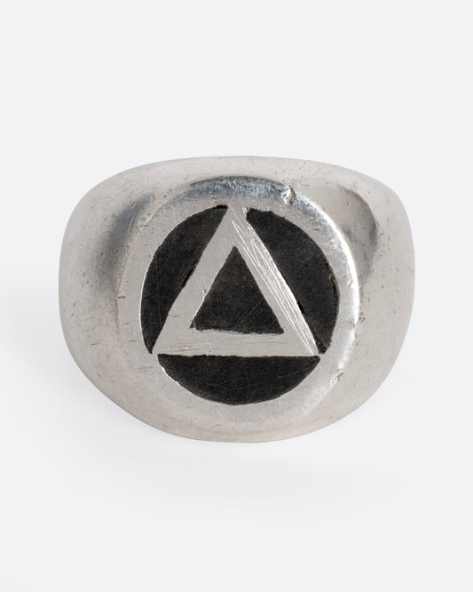 A silver signet ring with a black circle with a triangle at its center. Shown from the front.