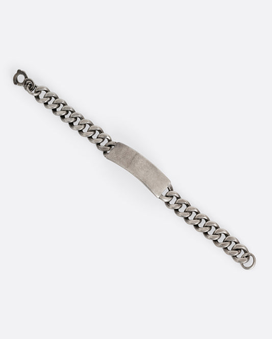 A silver cable chain ID bracelet with "A.R. Warren" in curling script  engraved on the inside of its name tag. Shown from the front.